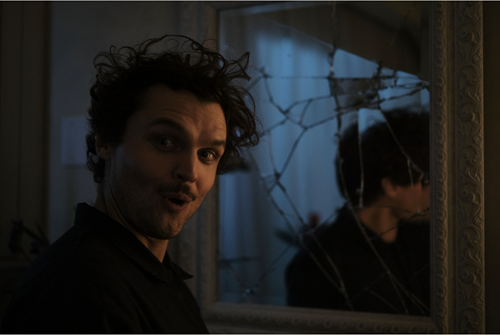 Ray Nicholson in the movie borderline standing in front of a broken mirror a he stares into the camera